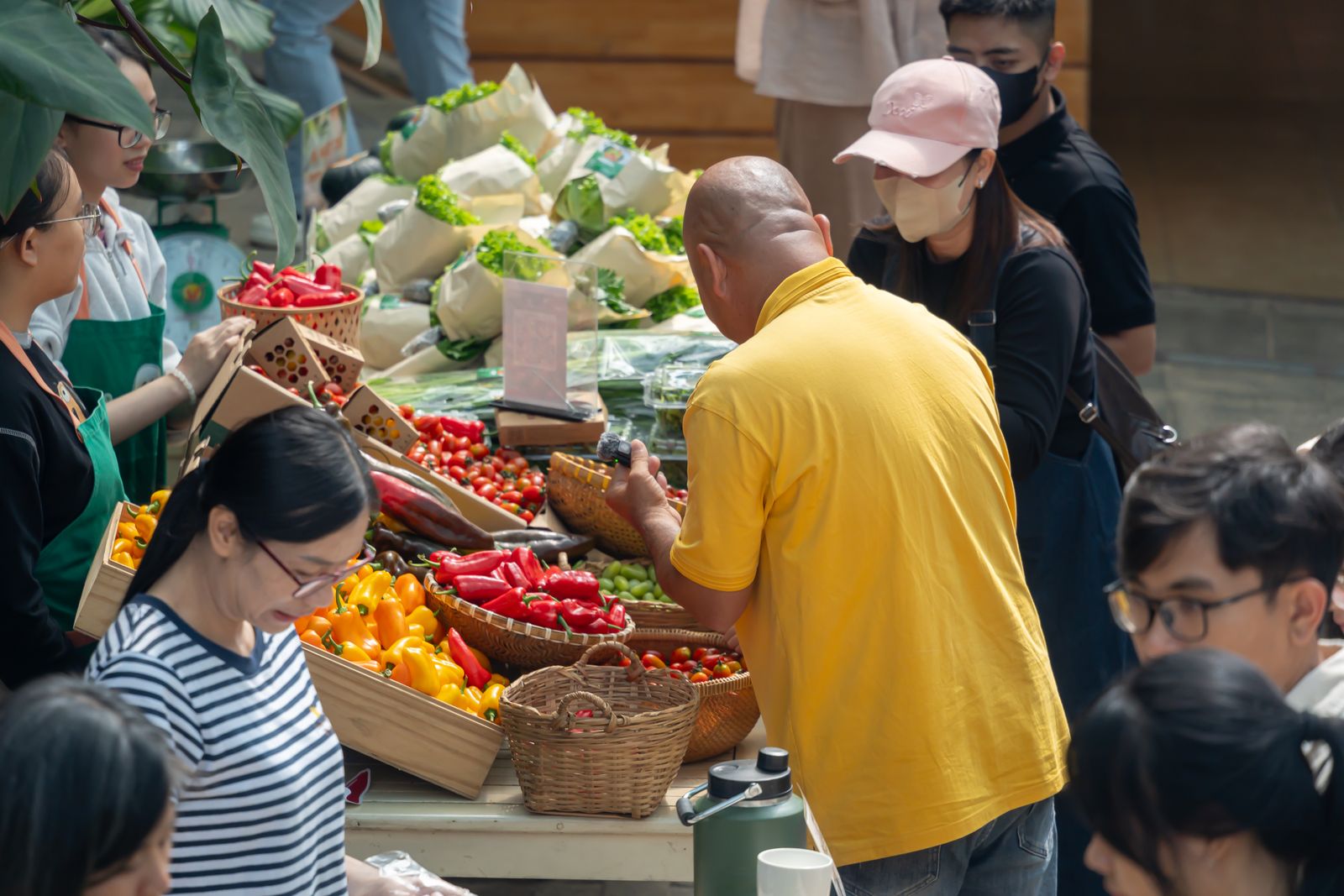 A diverse group of people shopping for fresh vegetables at an outdoor market, filled with colorful produce.