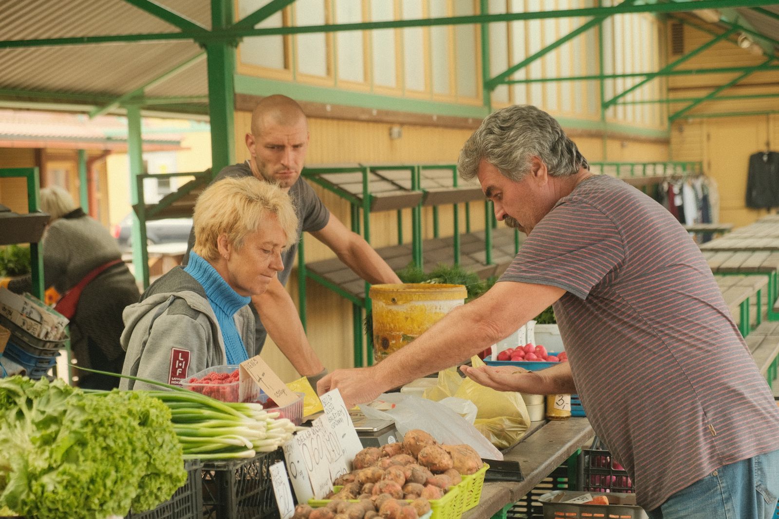 A farmer's market scene with vendors selling fresh produce including greens and potatoes.