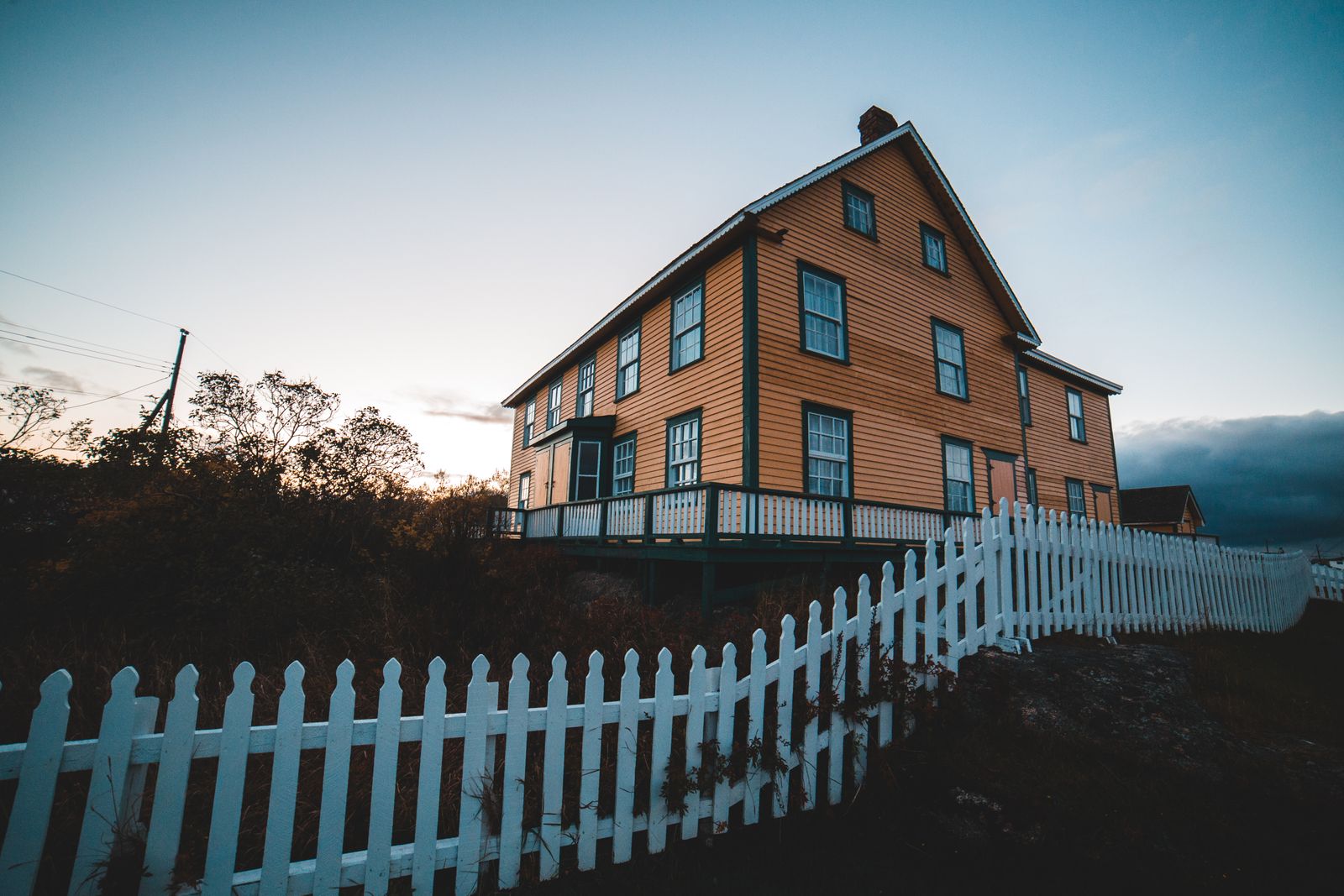 A picturesque wooden house with a white picket fence, captured at twilight, exuding warmth and charm.