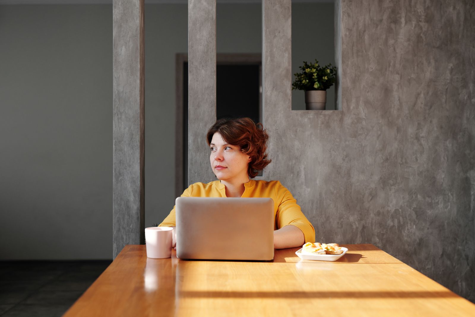 Woman working from home at a table, using a laptop and enjoying coffee and snacks.
