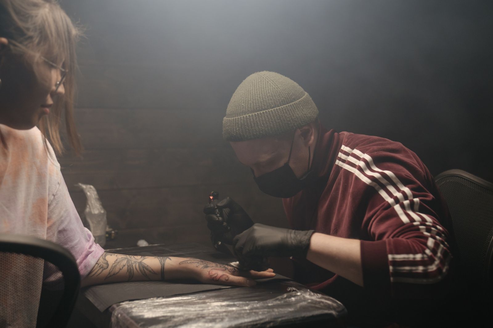 A tattoo artist inked in a studio, focusing on a detailed design on a client's arm.