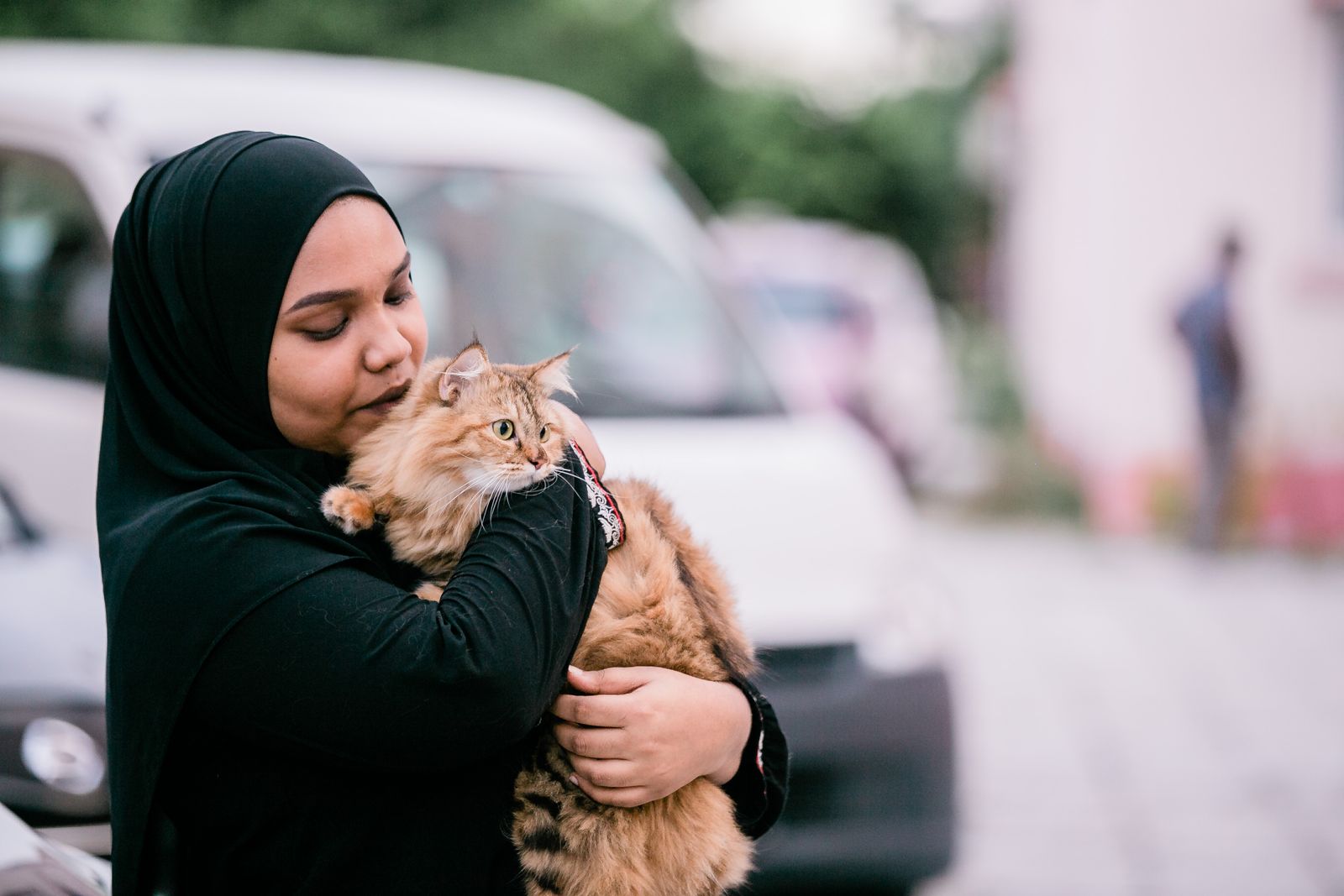 A woman in a hijab lovingly holds a fluffy tabby cat outdoors, showcasing companionship and affection.