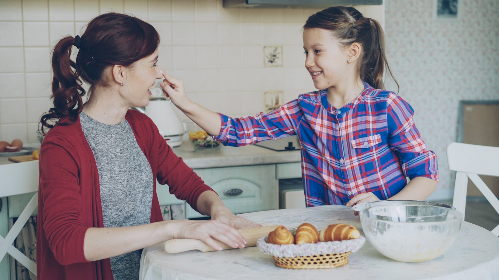 A girl puts flour on her mother's nose.