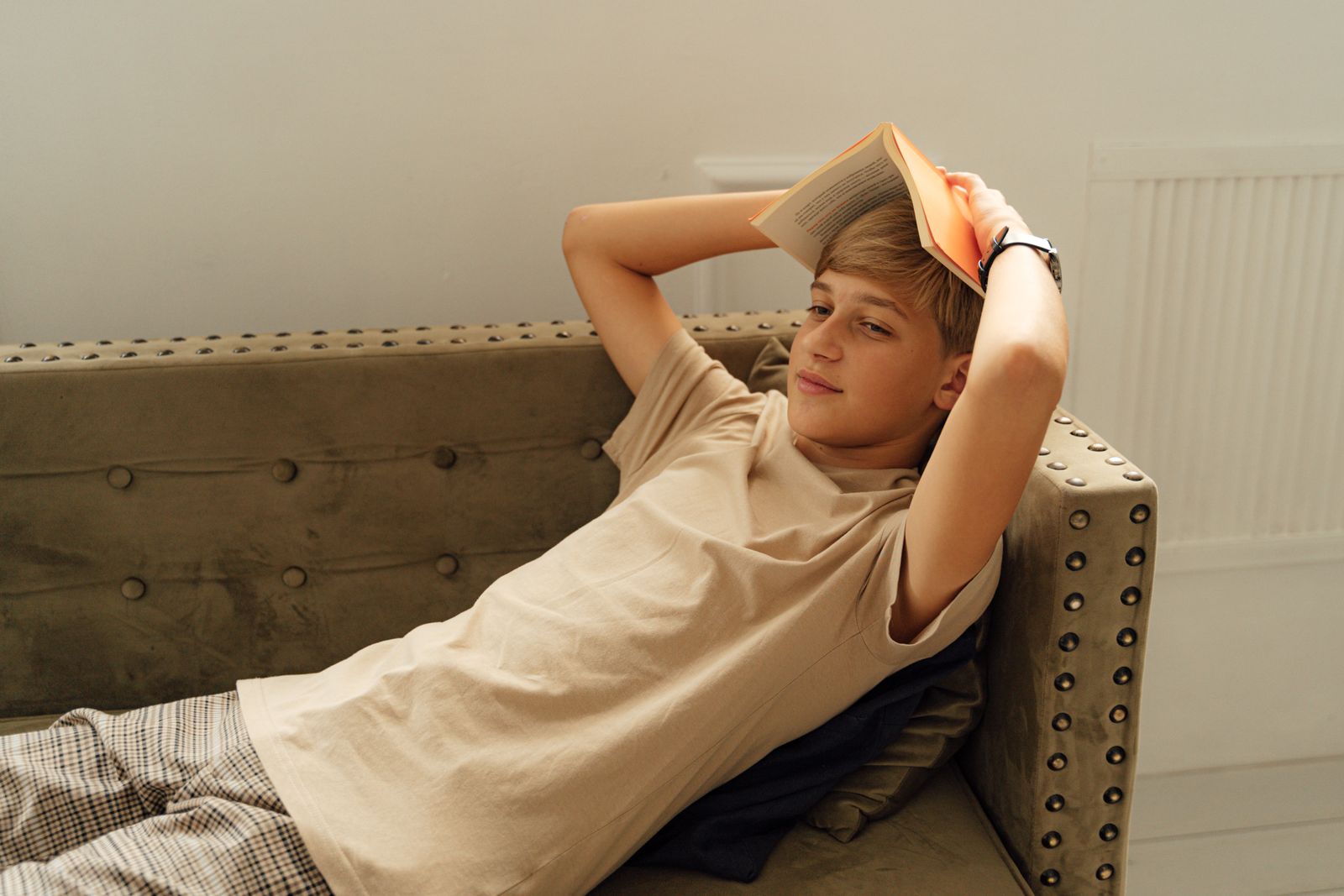 Teenage boy relaxing with a book on a sofa, enjoying a quiet indoor moment.