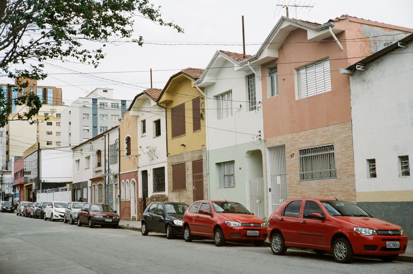 A row of colorful houses with cars parked along an urban street.