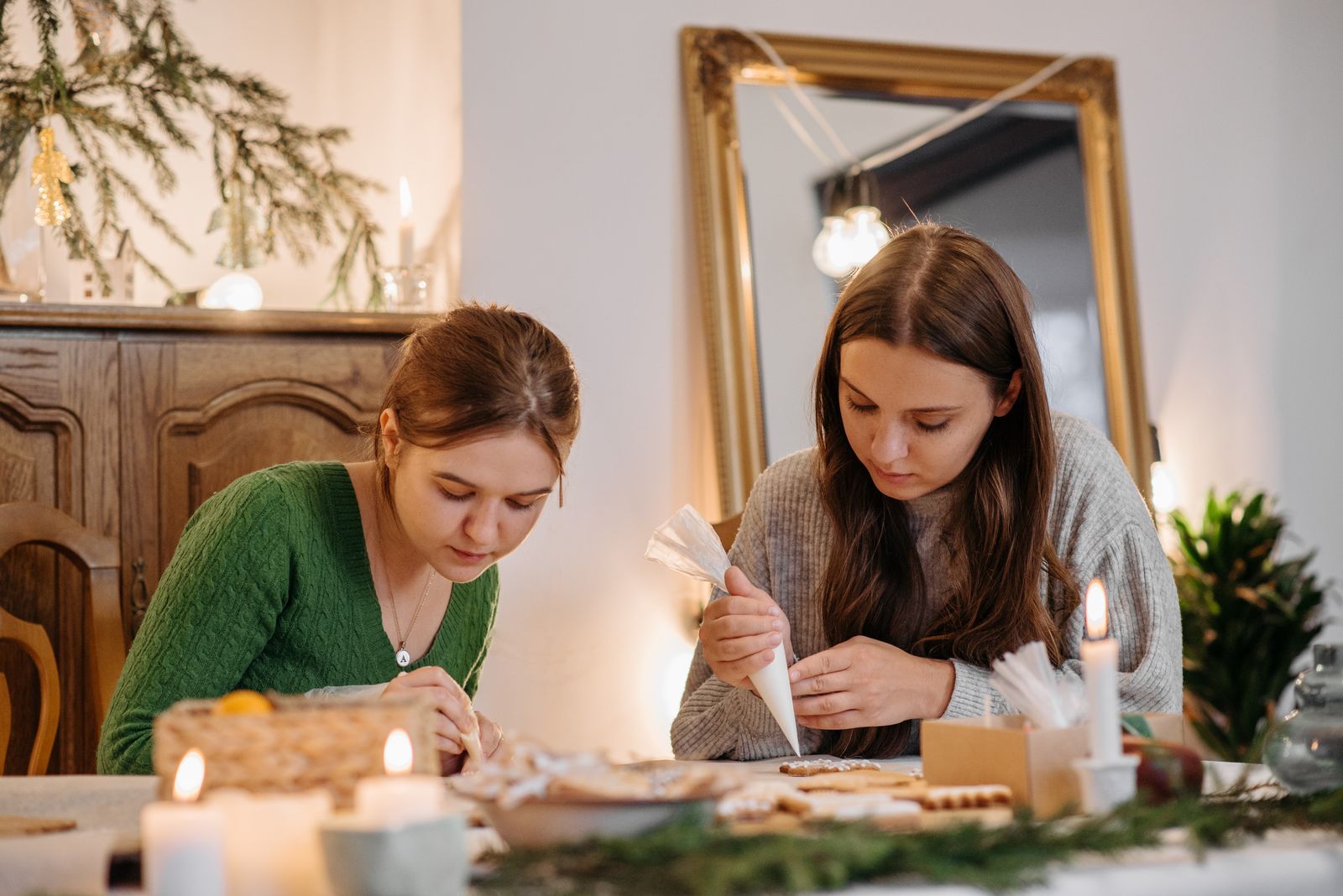 Two young women decorate cookies indoors during a festive Christmas gathering.