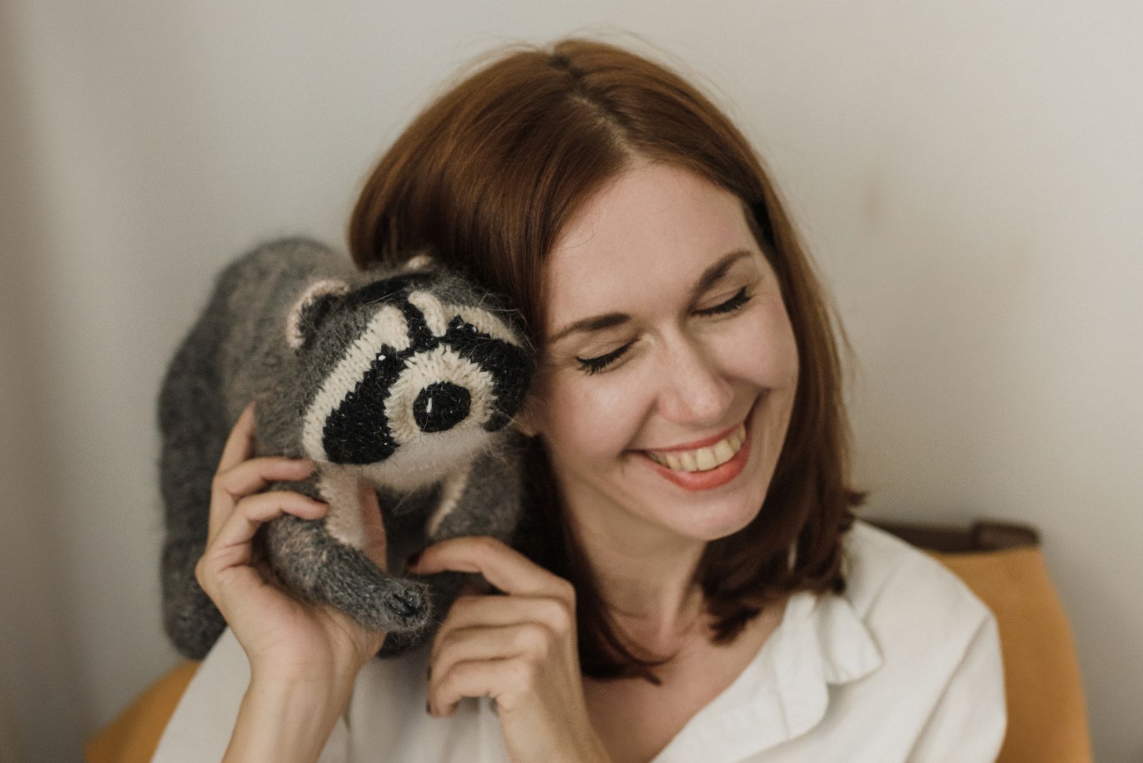 Smiling woman playfully holds a raccoon plush toy to her ear.