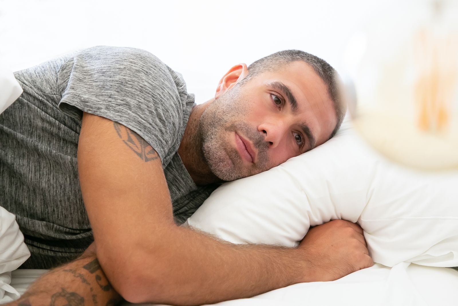 A man in a gray shirt lying on a pillow, reflecting on thoughts.