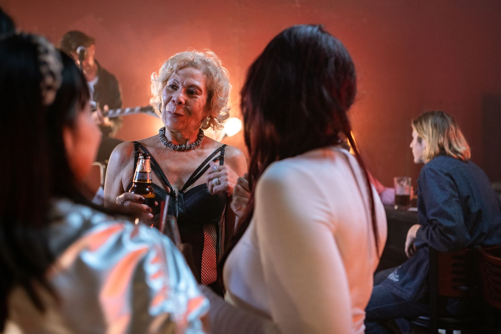 An elderly woman enjoys a vibrant night out at a bustling bar, socializing with friends.