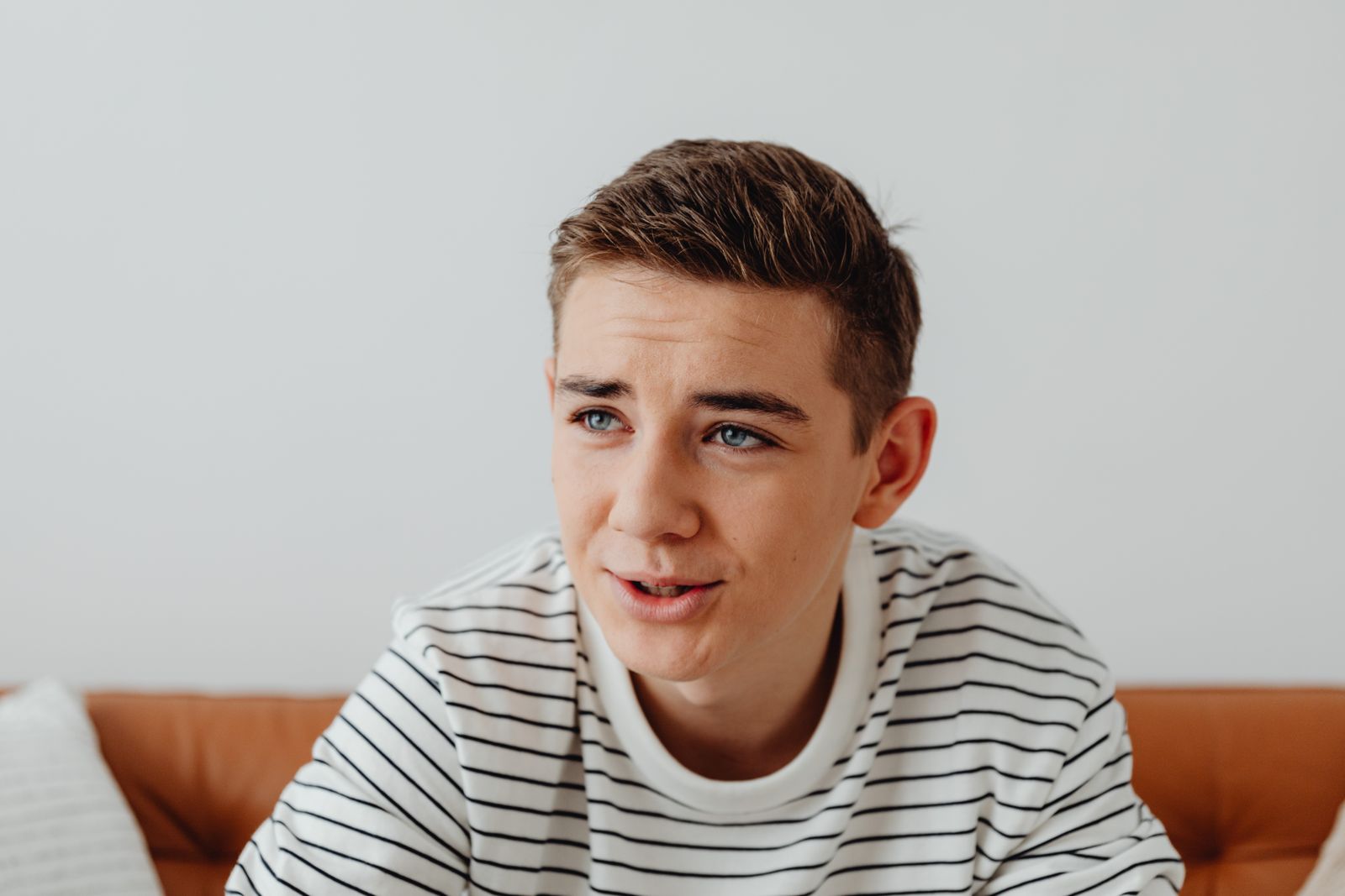 A young man in a striped shirt sits comfortably on a couch, looking engaged and thoughtful.