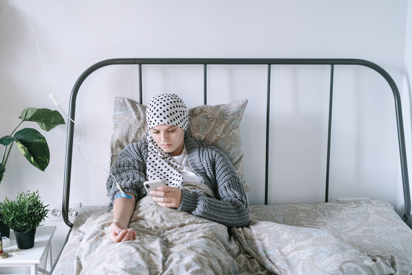 A woman undergoing chemotherapy checks her smartphone in a hospital bed, symbolizing hope and recovery.