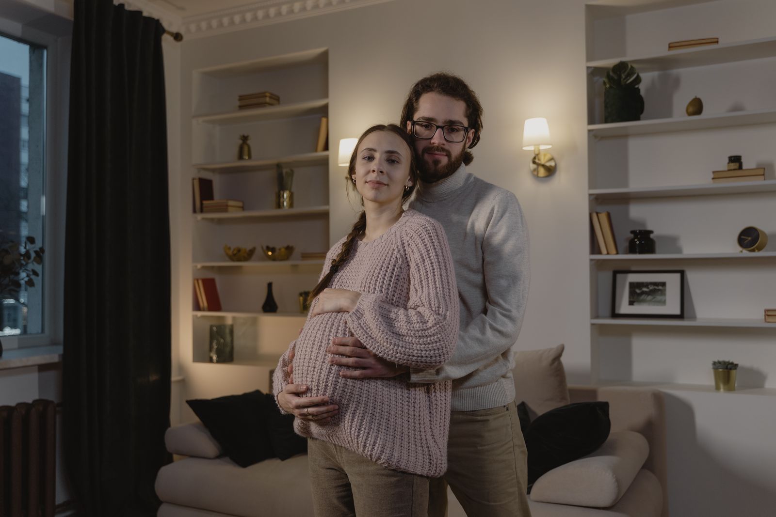 A loving couple standing indoors, expecting a child, with hands on the woman's pregnant belly.