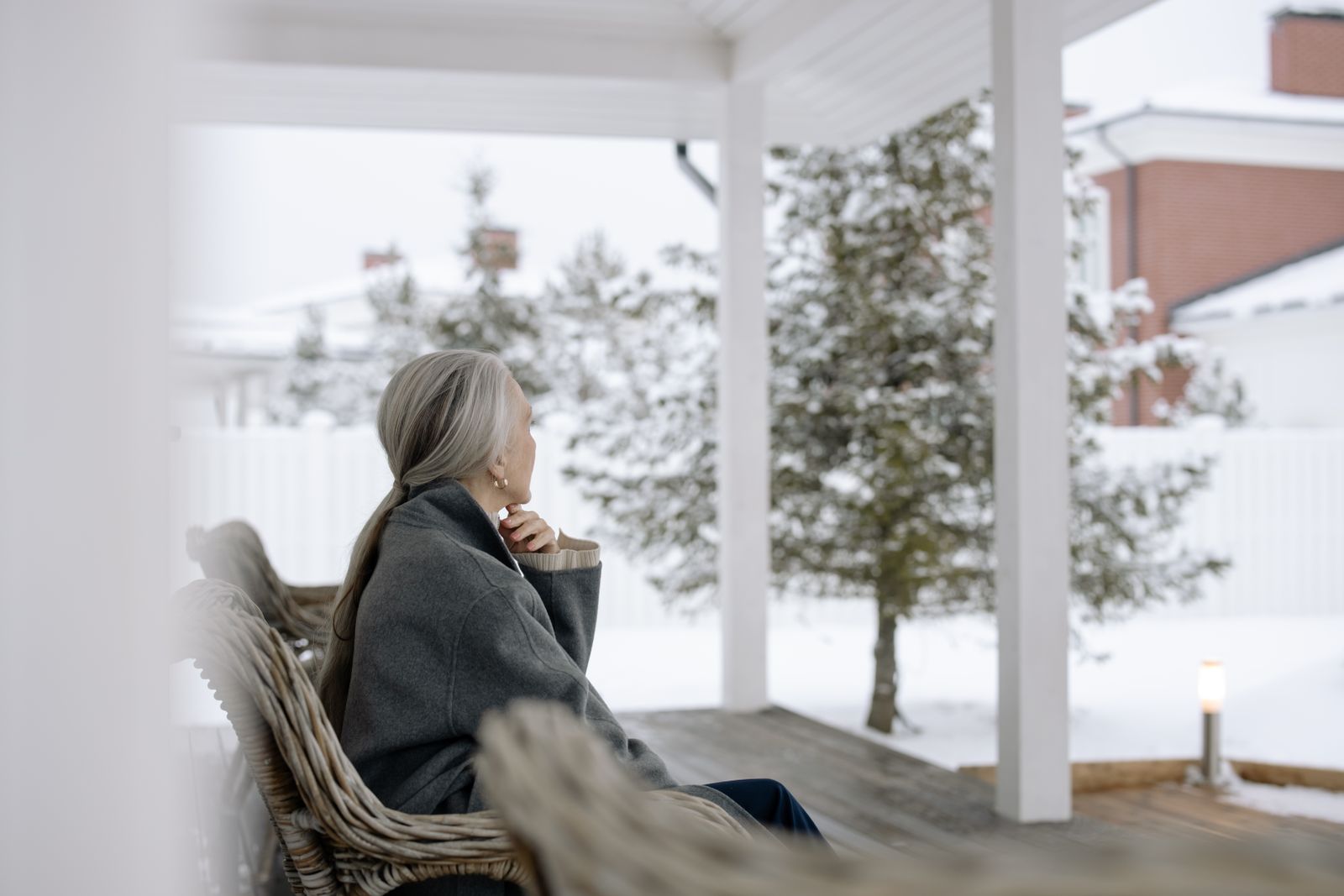 Senior woman sitting on porch in winter, enjoying serene snowy view.