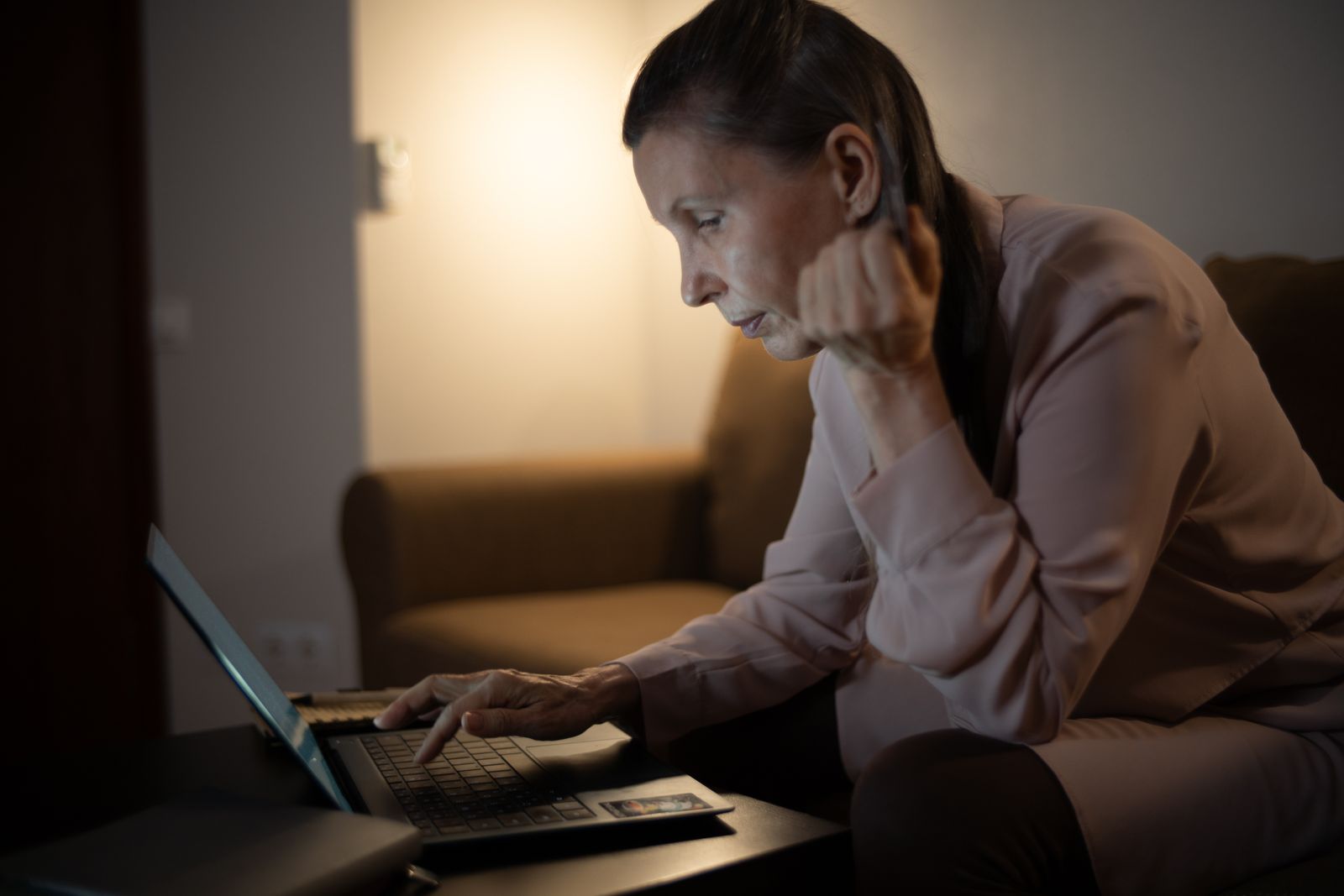 Senior woman using laptop in a dimly lit living room, focused on screen.