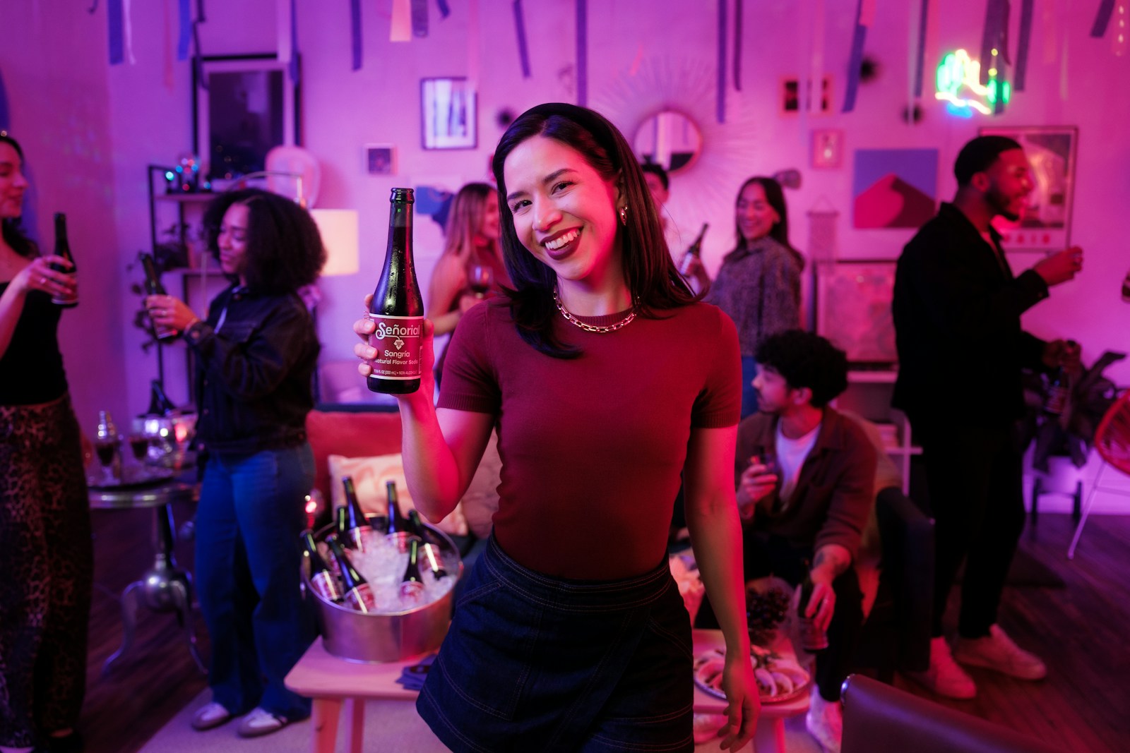 Woman smiles, holding a beer at a lively party.