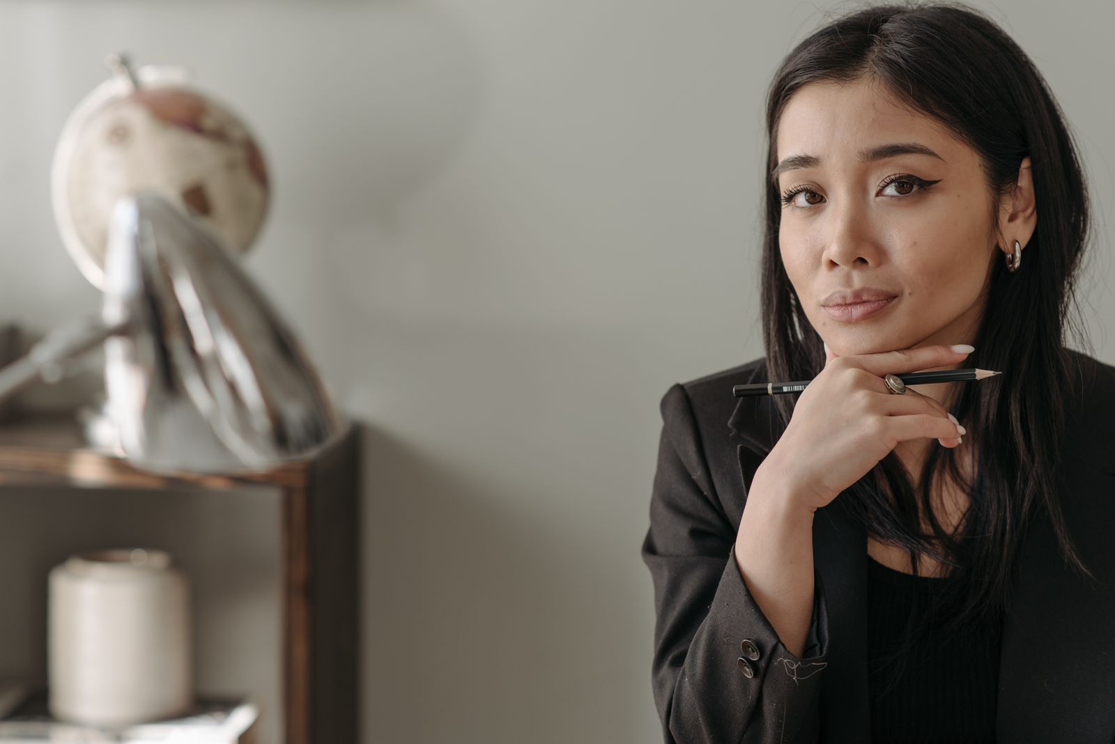 Confident woman in a black blazer holding a pen indoors, symbolizing focus and determination.