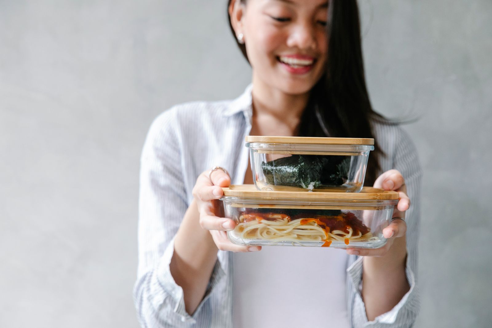 Crop happy ethnic female with onigiri and tasty noodle with sauce on white background