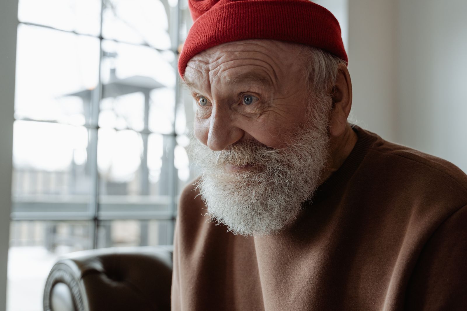 Charming portrait of an elderly man smiling with a red beanie, indoors.