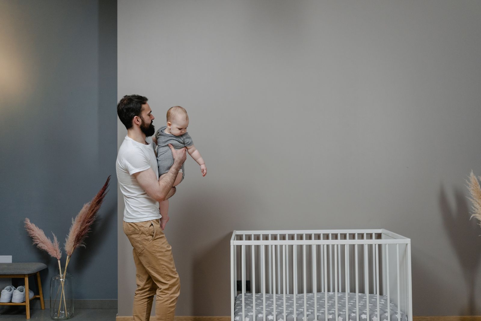 A father lovingly holds his baby near a minimalist crib in a cozy indoor space.