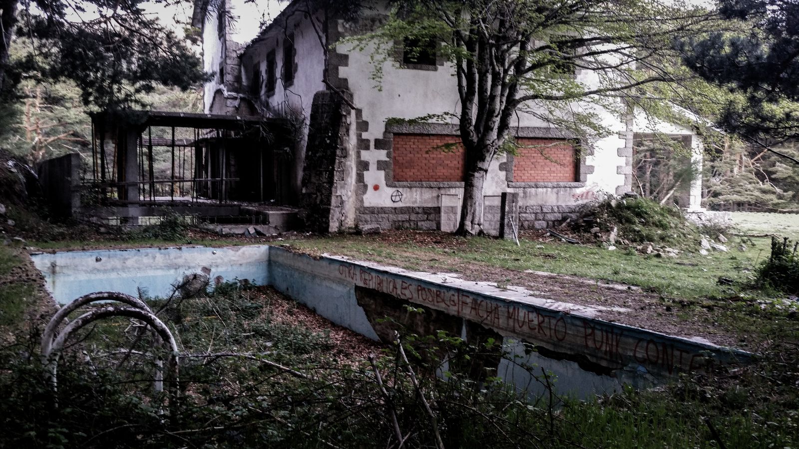 Dilapidated house with overgrown pool surrounded by forest, symbolizing decay.