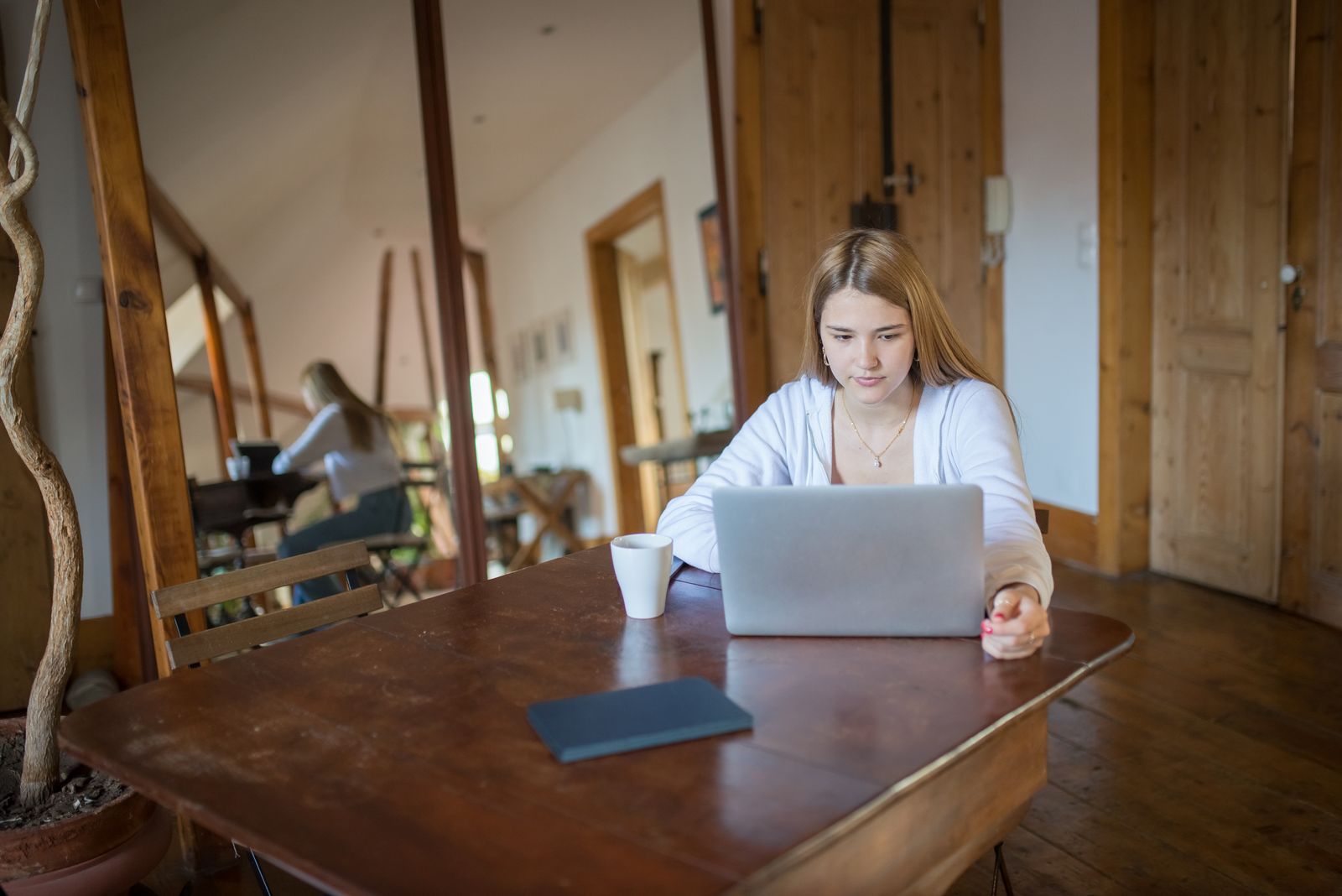 A young woman using a laptop indoors with natural wooden decor, creating a cozy workspace.