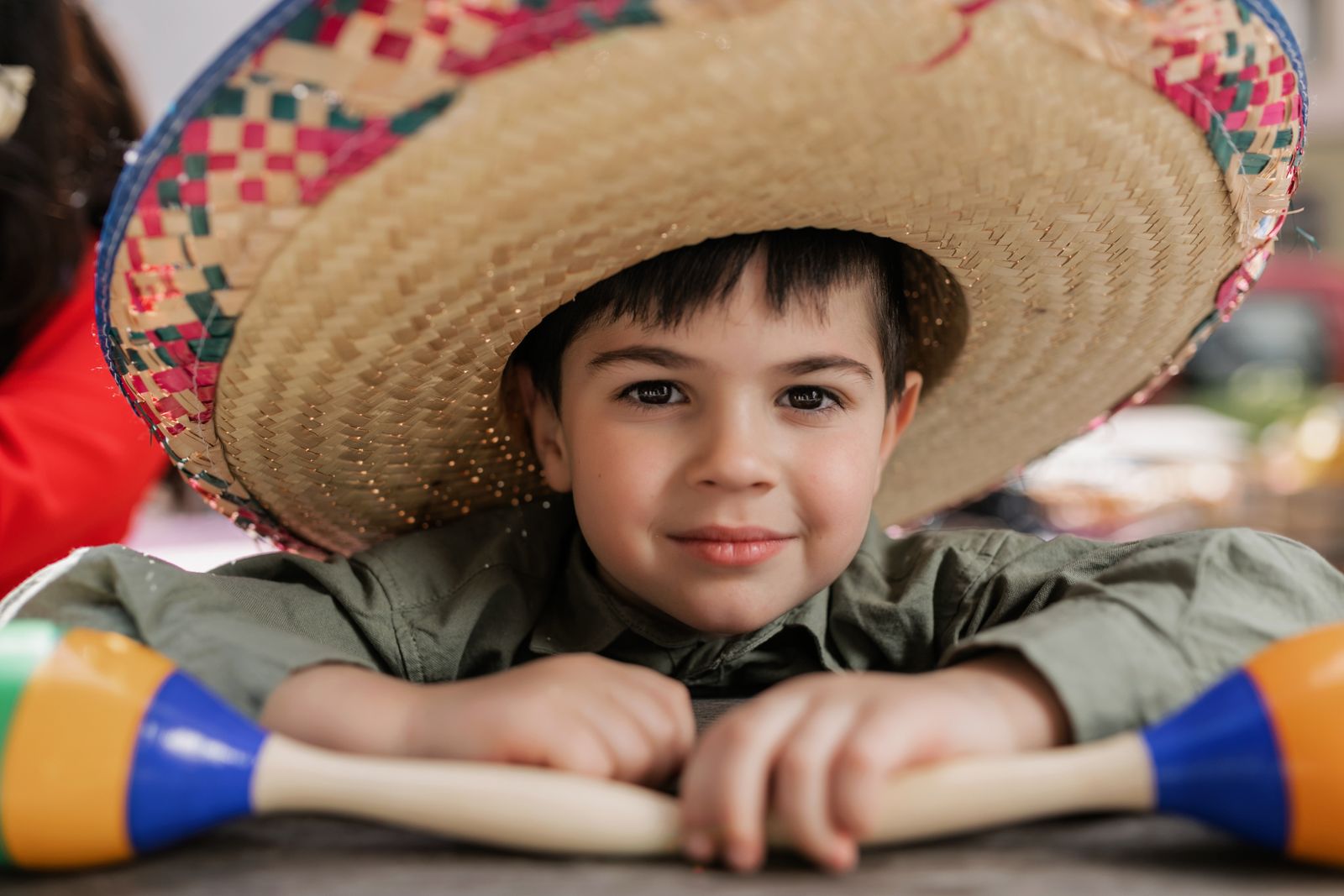 Child wearing a sombrero and smiling, holding maracas during a festive celebration.