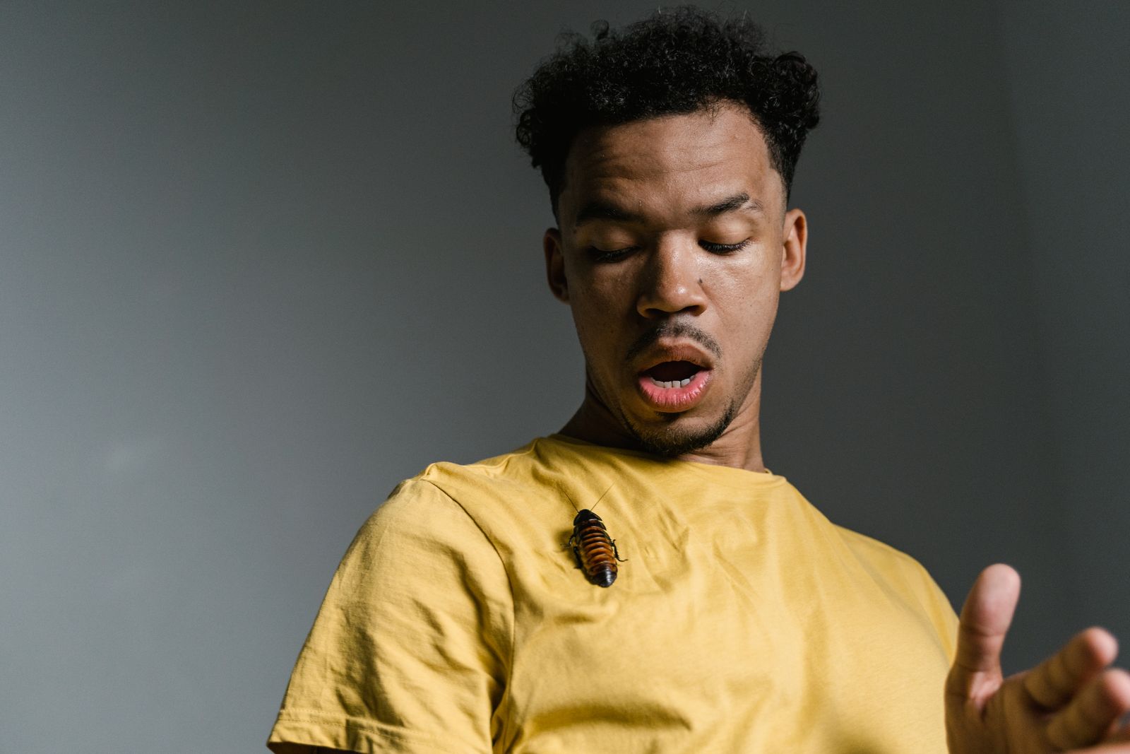 A man looks startled as a cockroach sits on his yellow shirt.