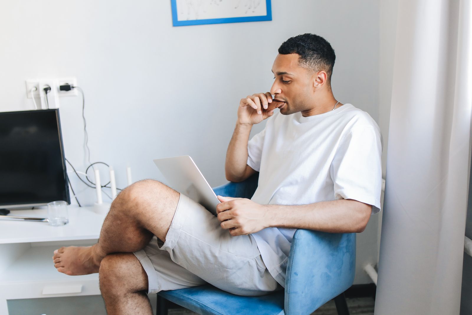 A man in casual clothes working remotely from home, seated in a cozy living room with a tablet.