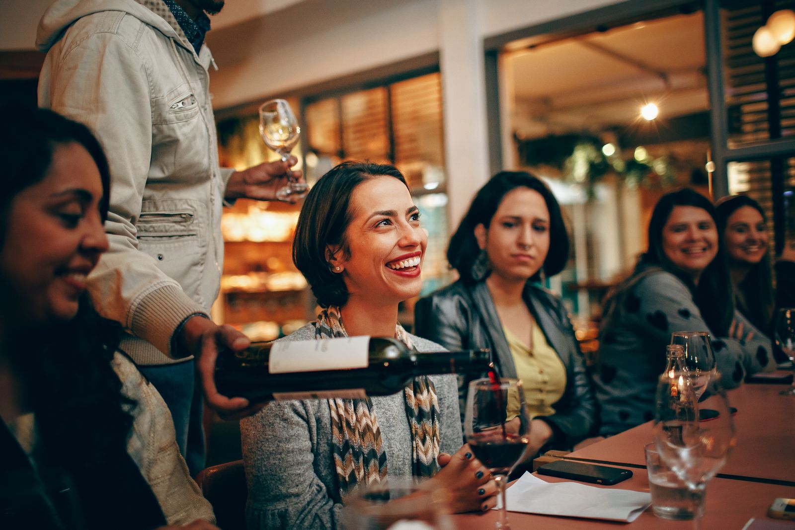 A cheerful group enjoys a wine tasting session in a warm, cozy restaurant atmosphere.