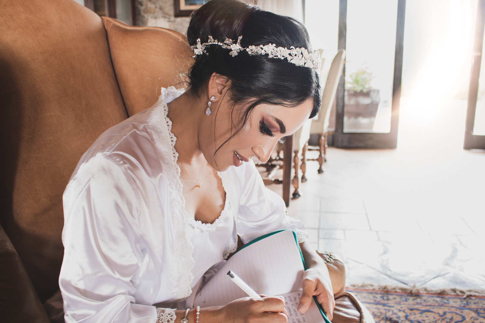 Bride in wedding robe writing notes in a notebook during her wedding morning preparation.