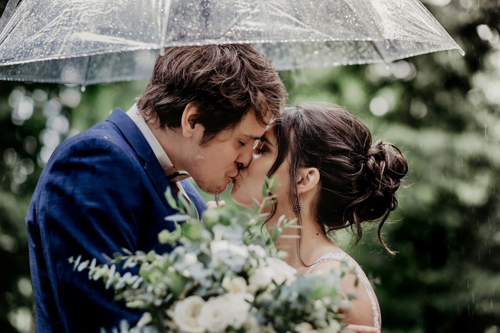 man in blue suit kissing woman in white floral dress