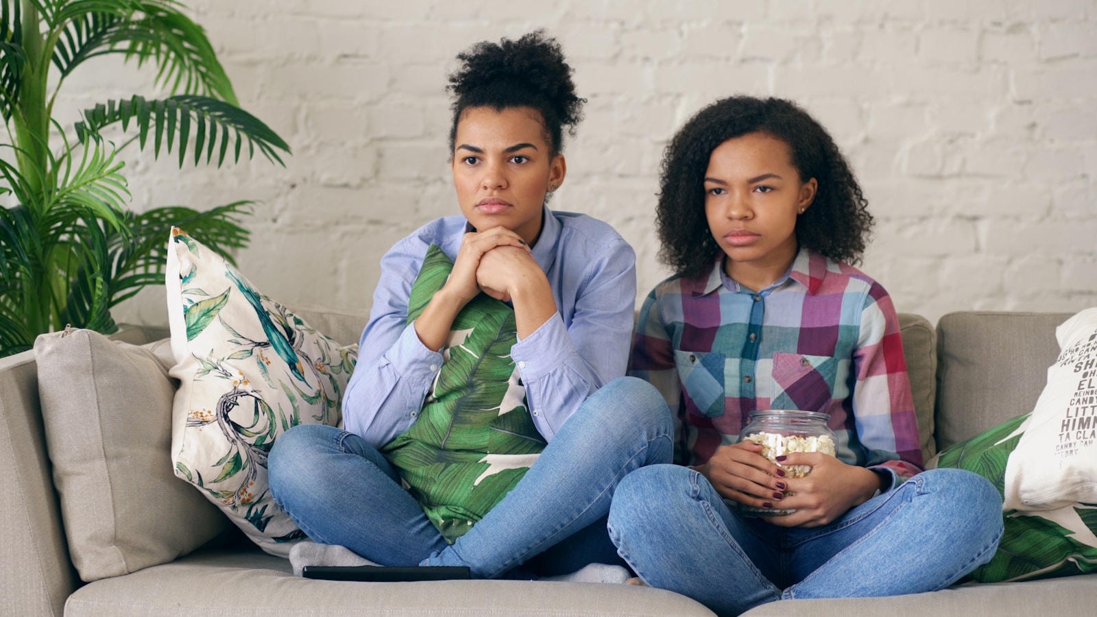 Two women sitting on a couch watching television.