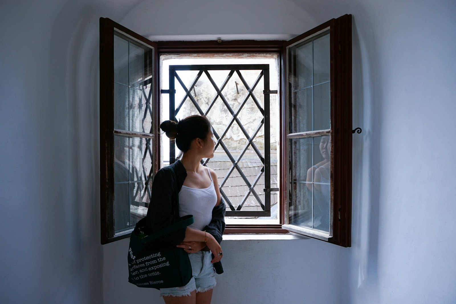 woman in black tank top and white pants standing beside window