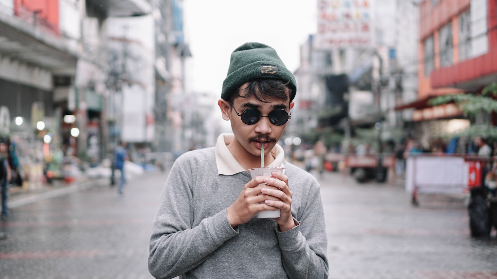 a man in a hat and sunglasses holding a drink