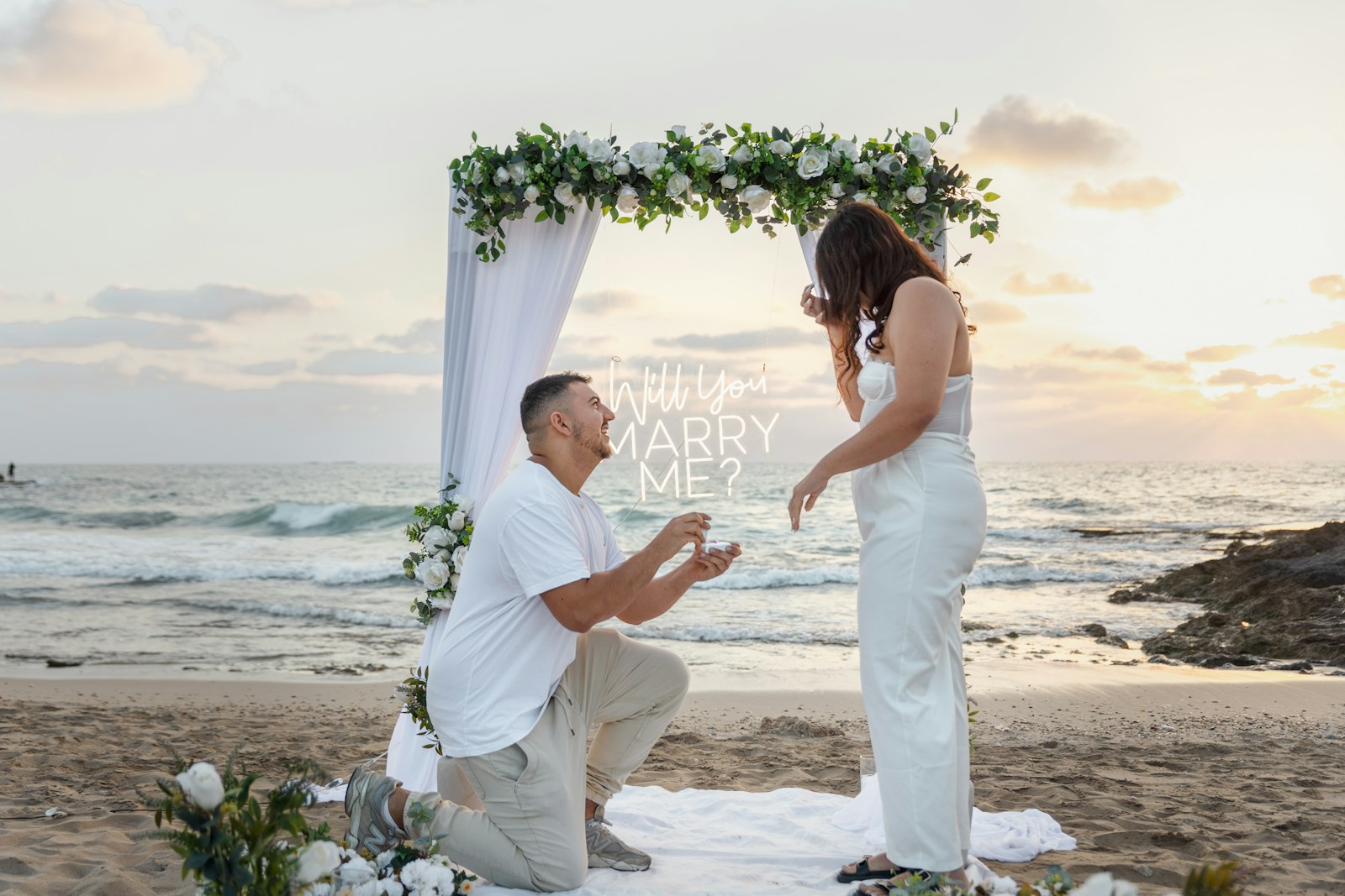 Man proposes to woman on beach at sunset.