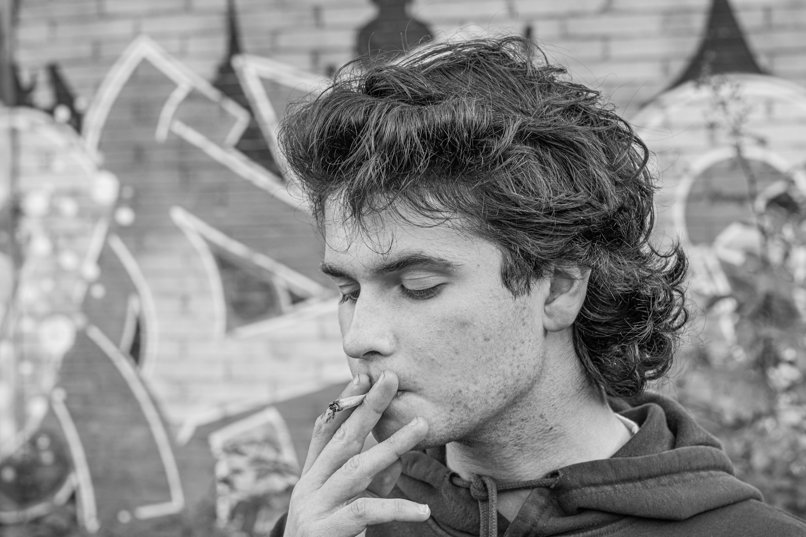 a man smoking a cigarette in front of a graffiti wall