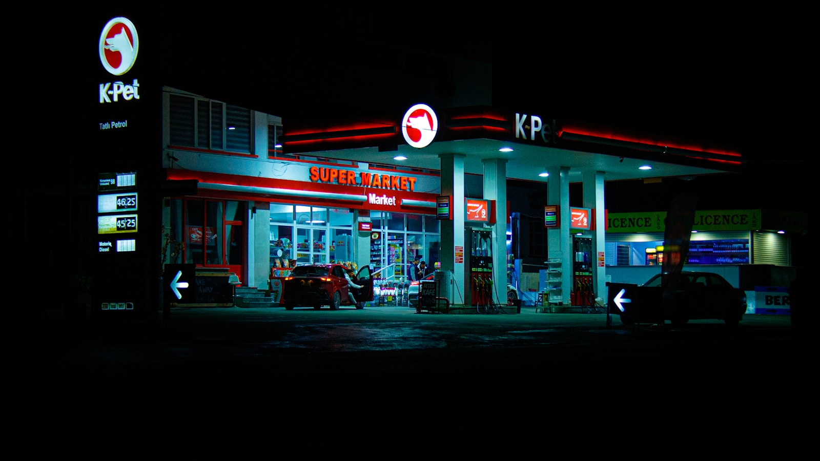 Gas station illuminated at night with cars present cars