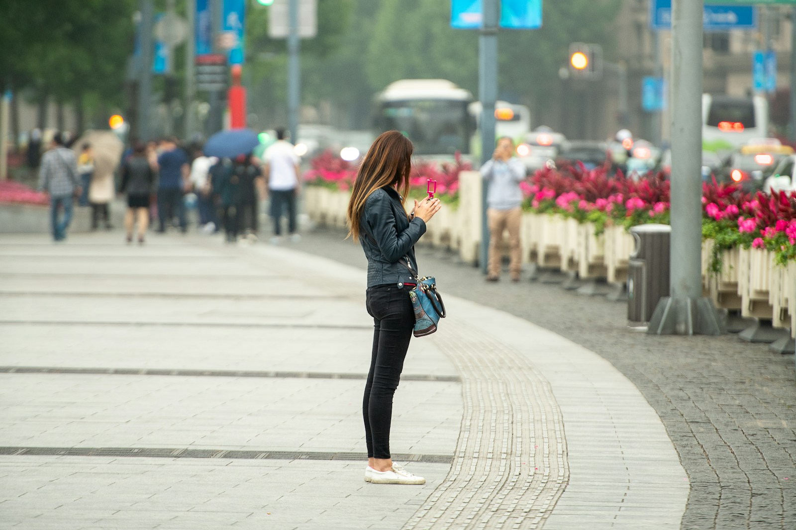 A woman stands on a city sidewalk using her phone.