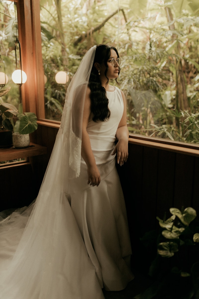 A bride in a white dress looks out a window