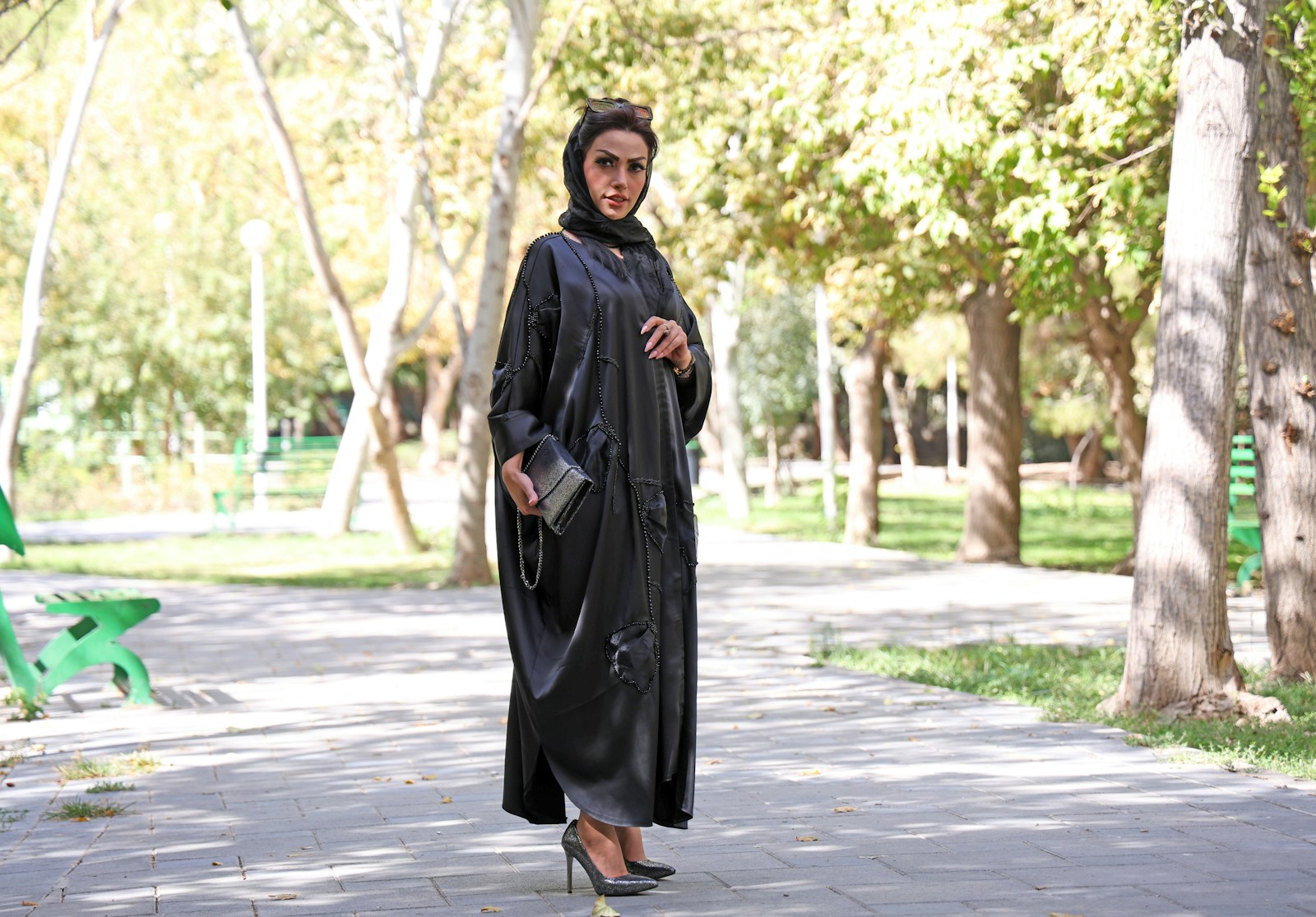 Woman in black abaya and hijab poses in park.