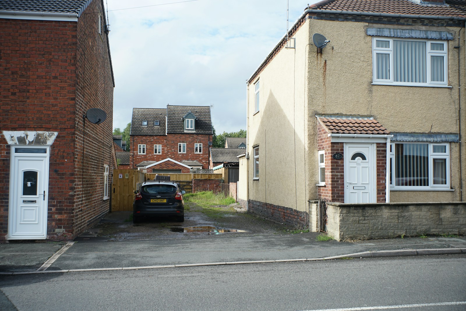 Two houses flank a drive with a parked black car.