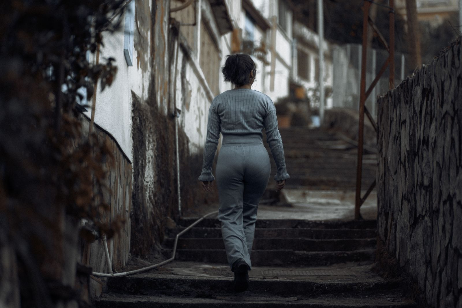 A woman in casual attire walks up concrete steps in a gritty urban environment, ideal for themes of solitude and determination.