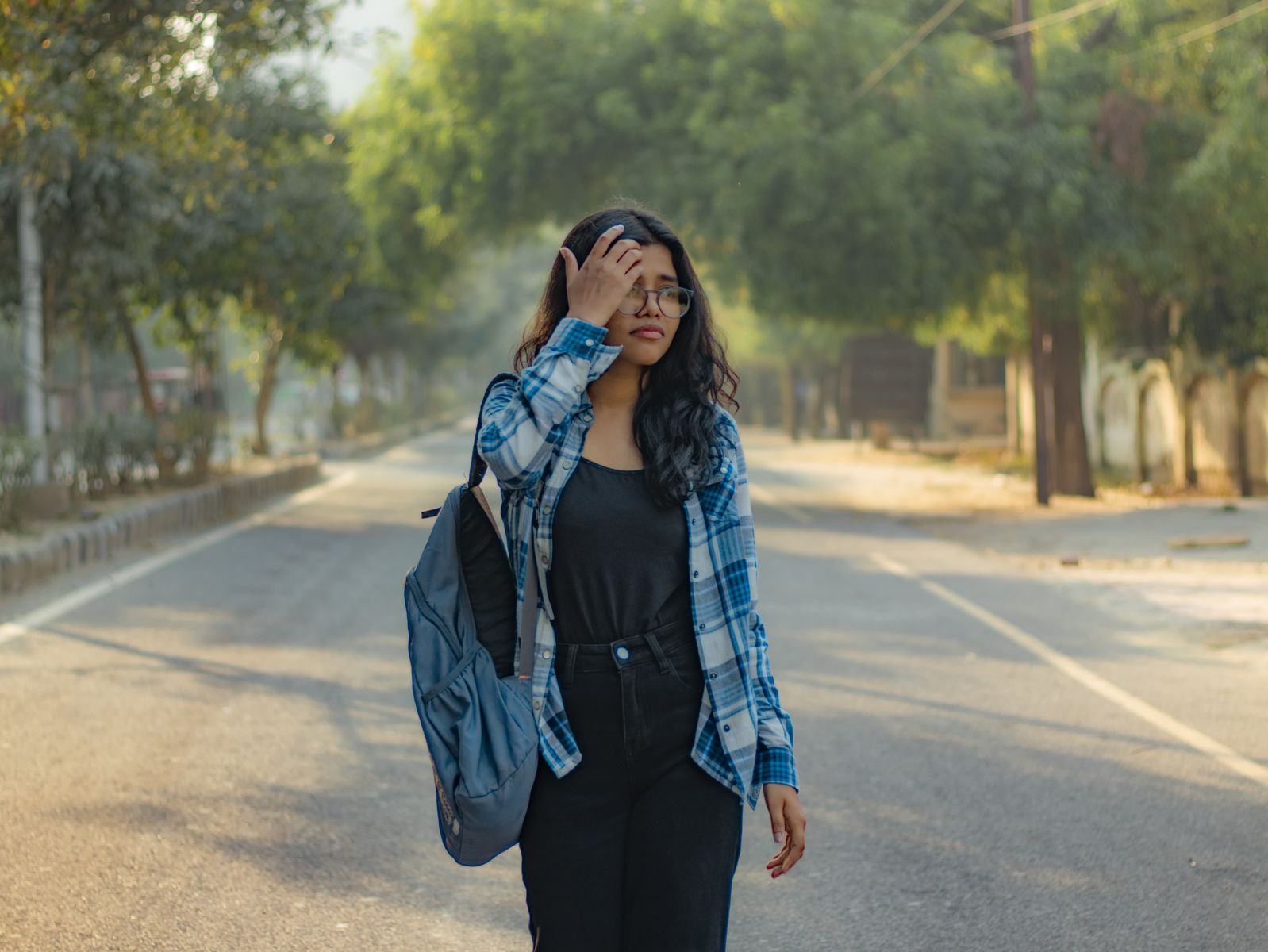 A young woman in casual attire walks along a sunny park road, enjoying a serene day outdoors.
