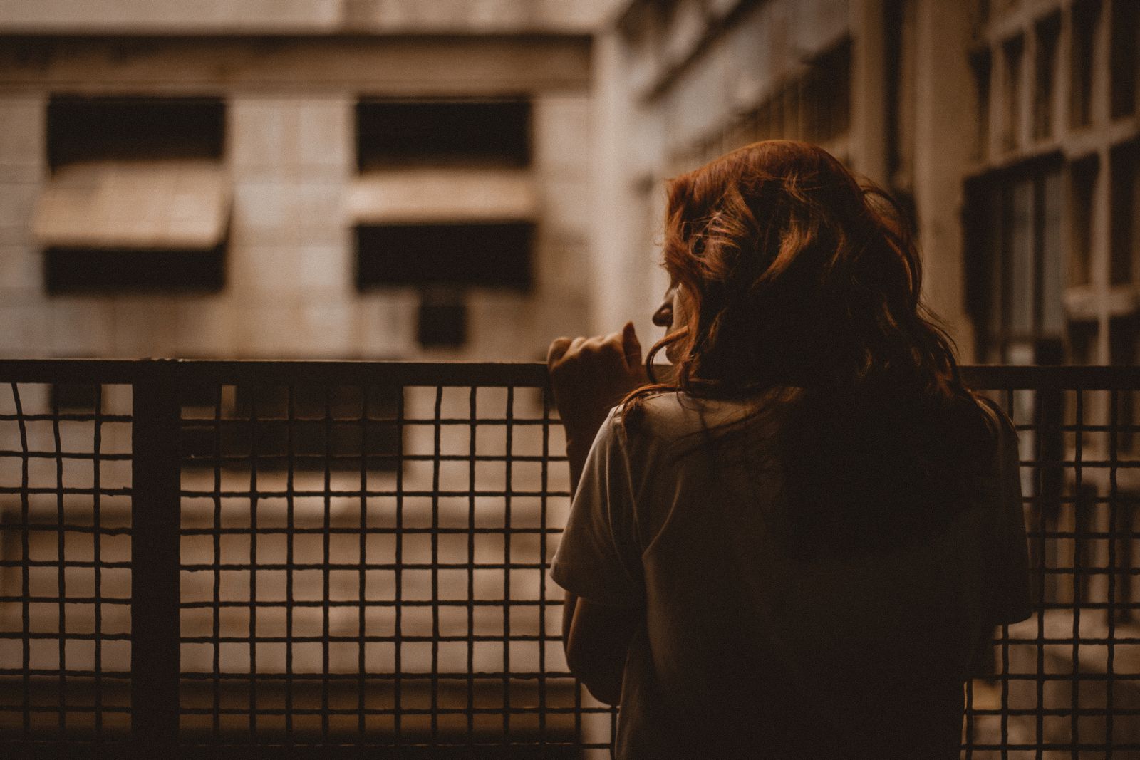 A woman stands alone looking through a railing with a sepia-toned, contemplative mood.