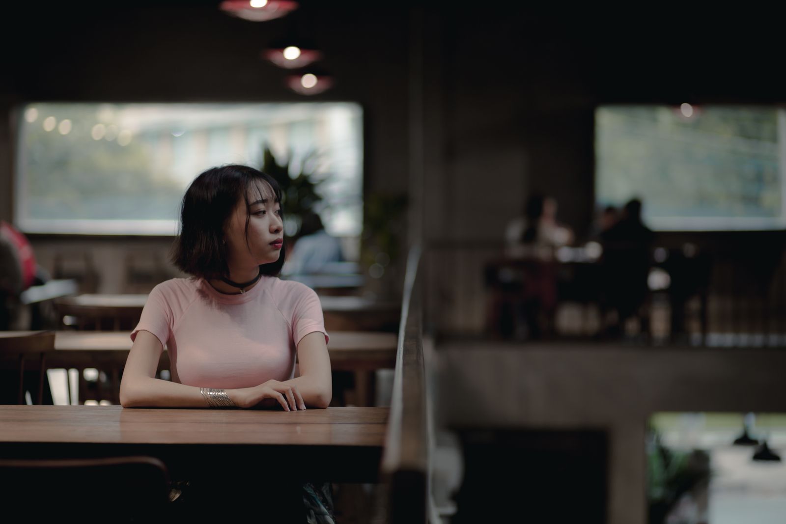 Woman in pink shirt seated alone in a stylish cafe, thoughtful atmosphere.