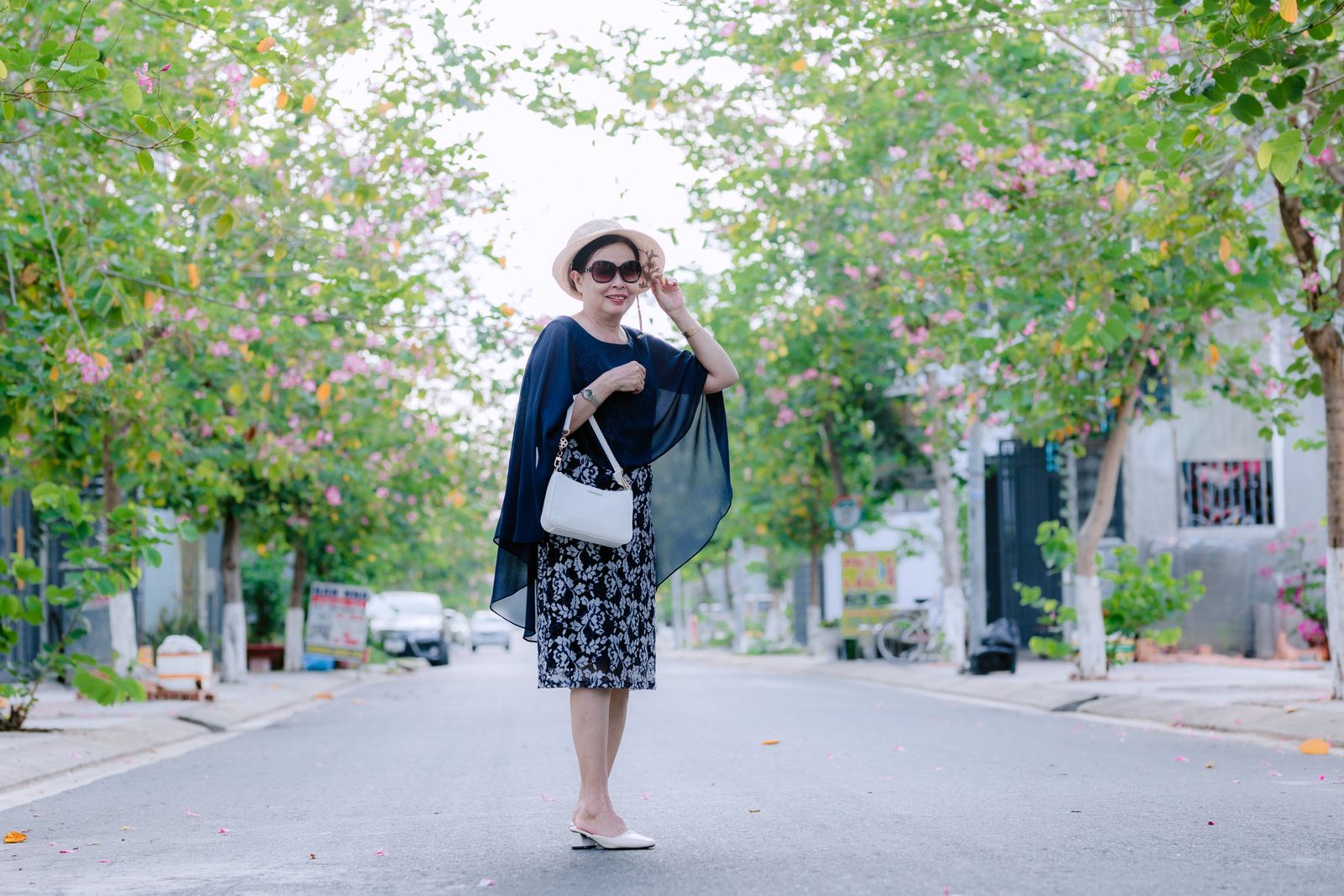 Smiling woman in summer outfit strolling through a vibrant green street.