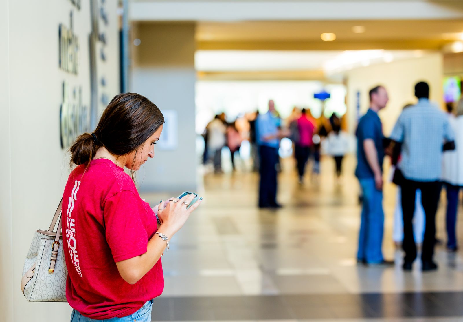 Young woman texting on smartphone in a bustling indoor corridor.