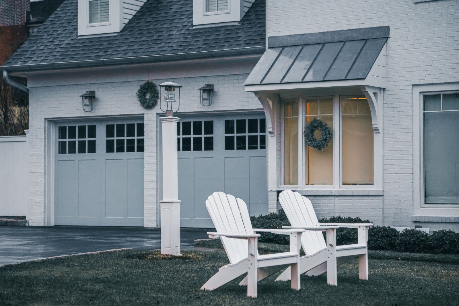 Two white Adirondack chairs in front of a cozy suburban home.