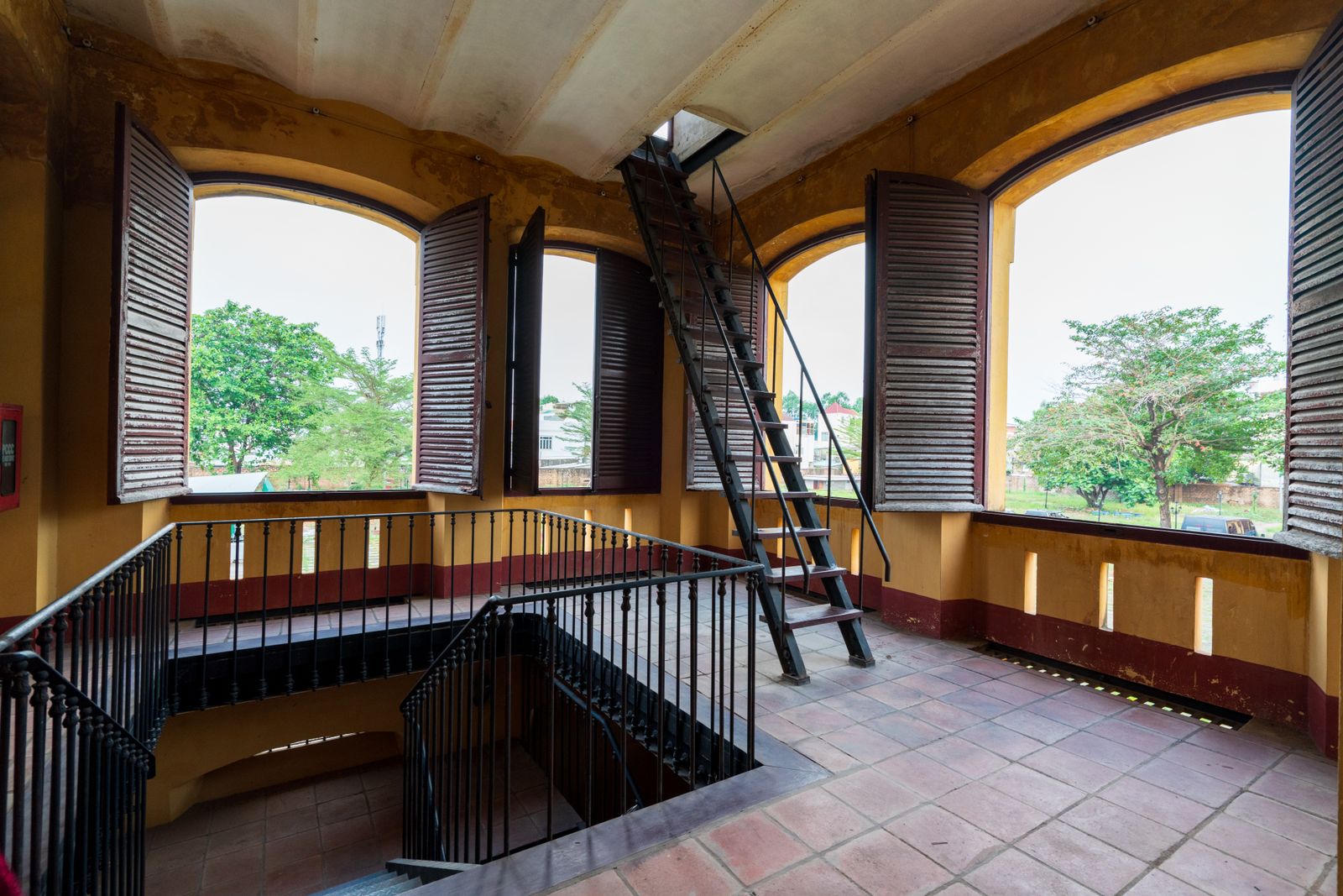 Rustic interior of a historic building with wooden shutters and a metal staircase leading to the attic.
