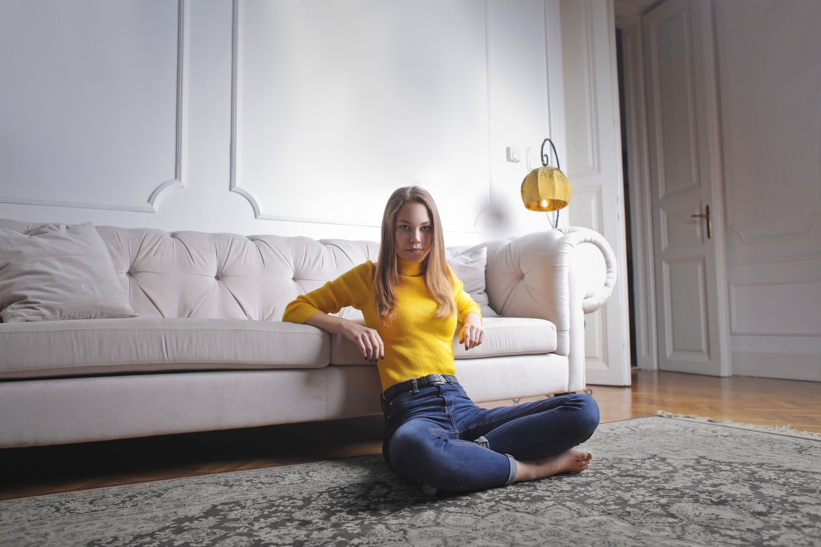 A young woman in a yellow sweater sitting on the floor in a stylish modern living room. Perfect for lifestyle themes.